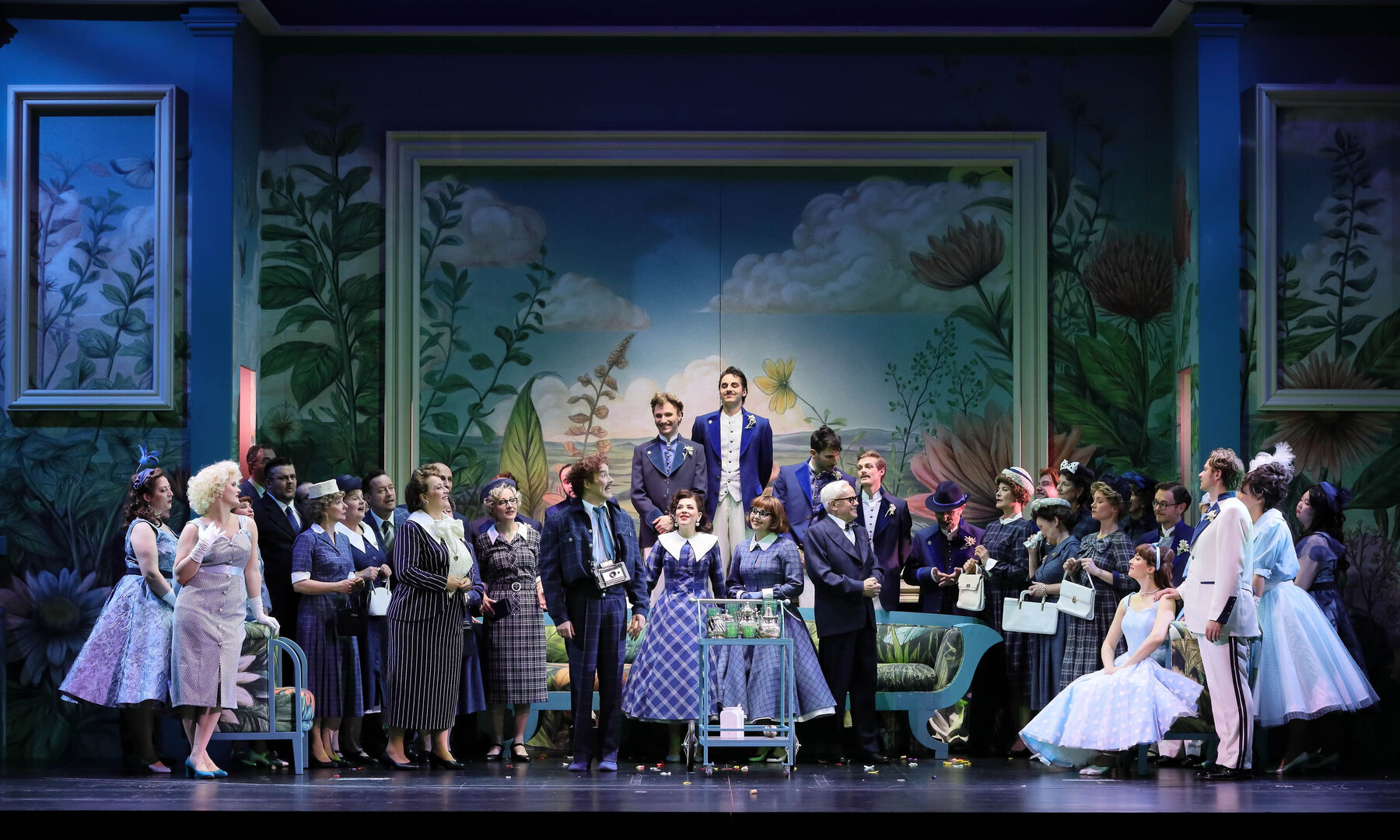 The ensemble stands, or rather sits, lined up in front of a serving trolley with several teapots and green glasses. The mood is partly exuberant, partly sceptical.
