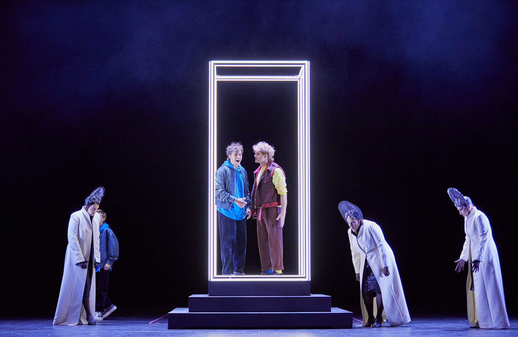 Tamino und Papageno sind in der Prüfung gefangen. Sie stehen in einem leuchtenden Quader auf einem Podest. Papageno schaut den rufenden Tamino fragend an. Die drei Damen nähern sich wütend.