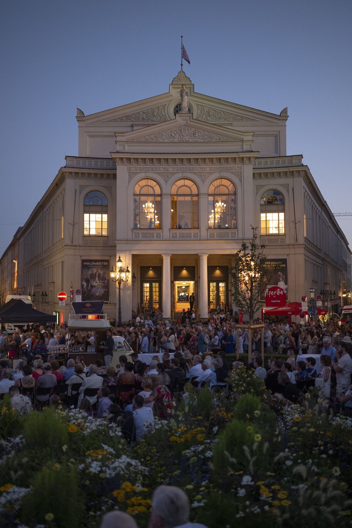 Das Gärtnerplatztheater in Abendlicht. Davor sitzen und stehen viele Menschen.