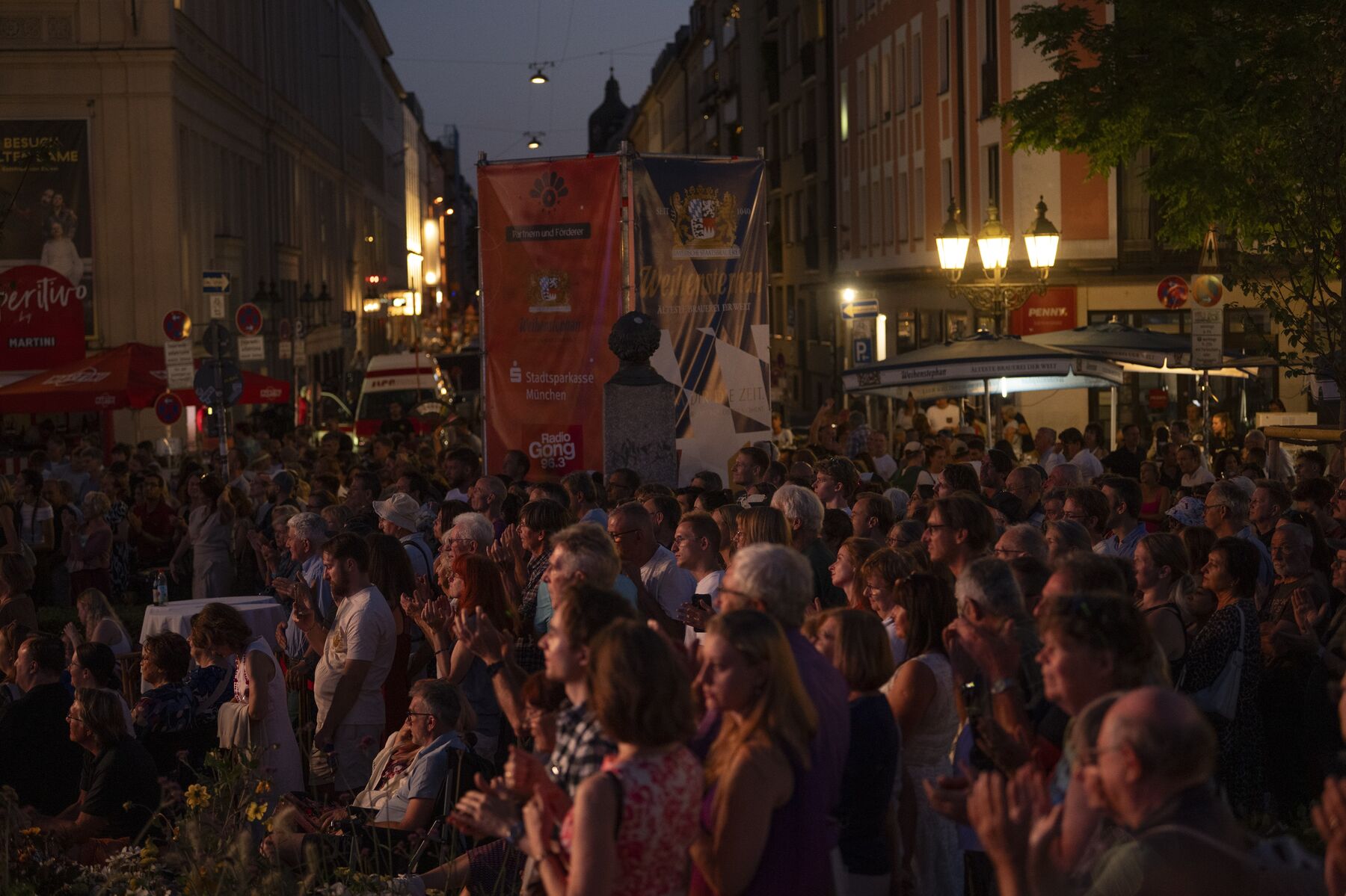Eine Menschenmenge im Abendlicht schaut gebannt auf eine Bühne.