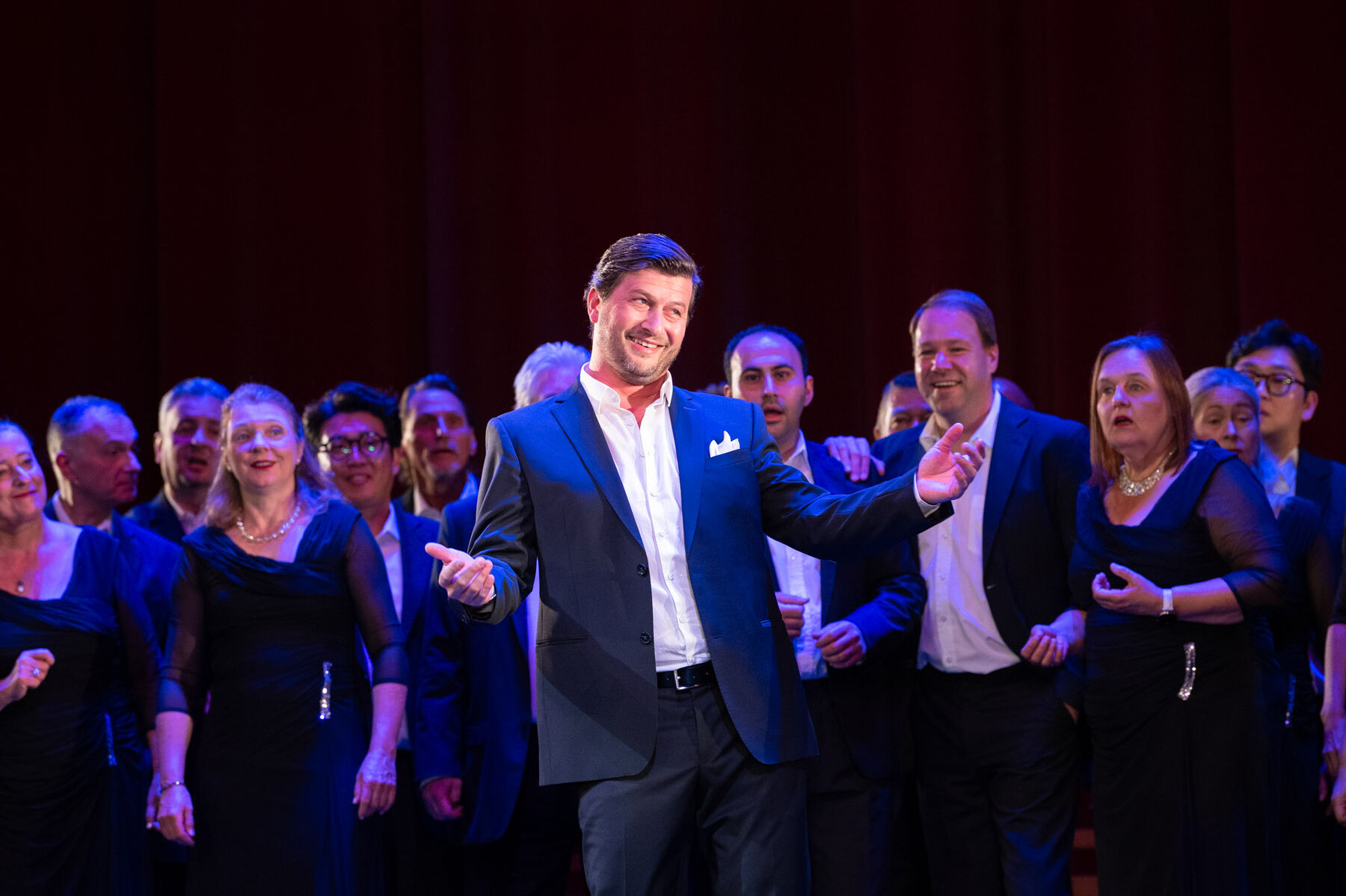  Levente Páll steht auf der Bühne und singt, hinter ihm der Chor