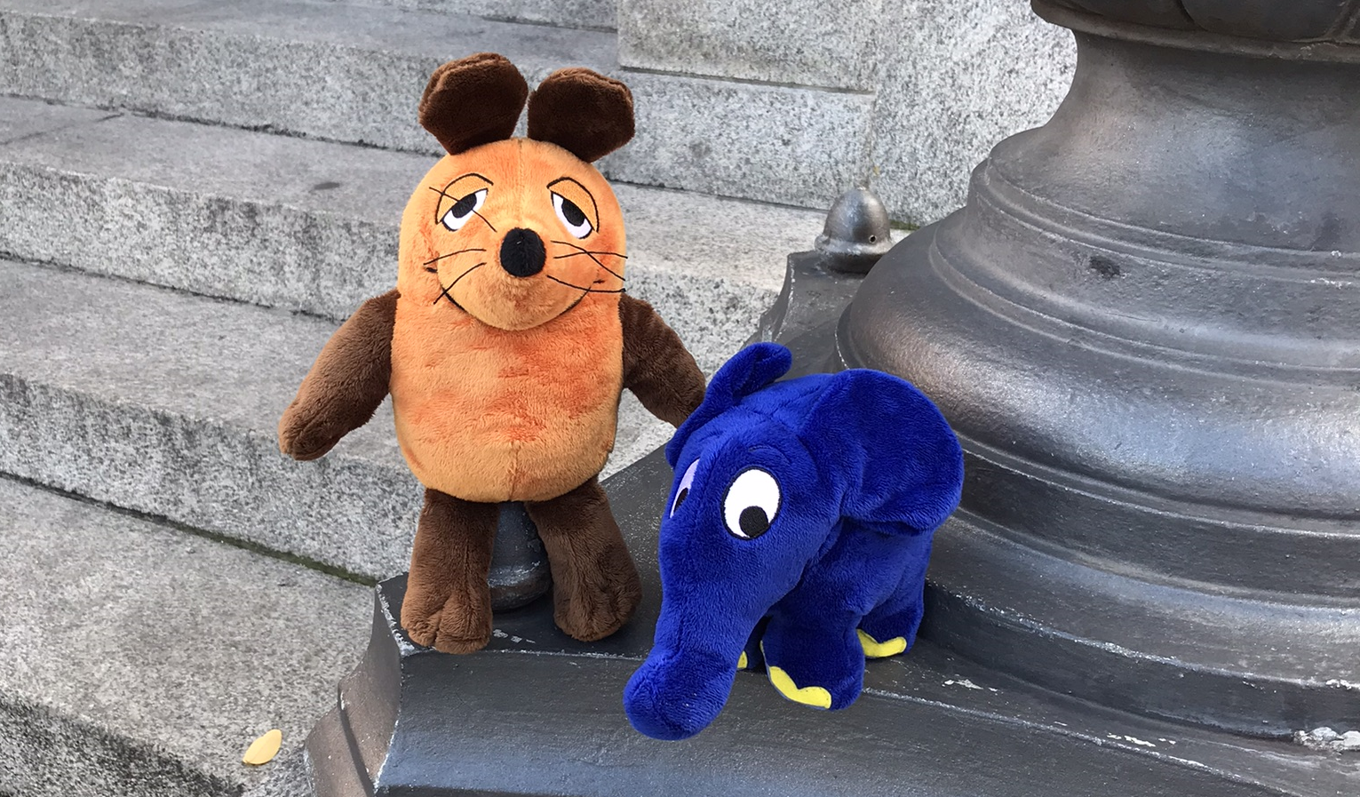 Eine Kuscheltier-Maus und ein Kuscheltier-Elefant stehen auf den Stufen des Gärtnerplatztheaters.